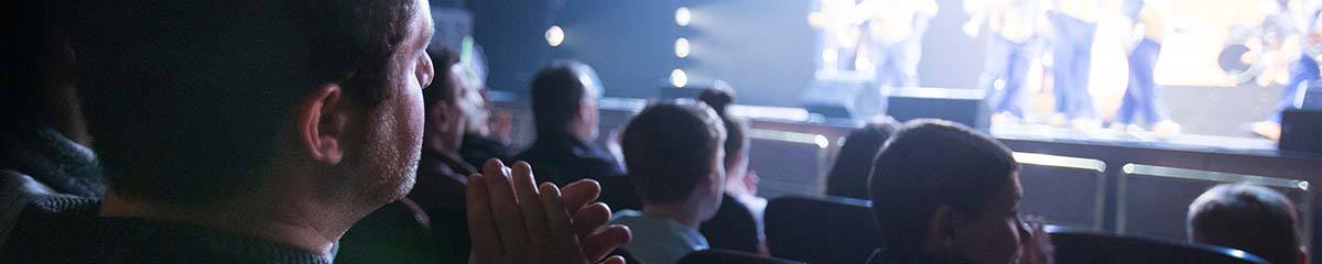 A theater goer claps in their seat as they watch a performance on stage