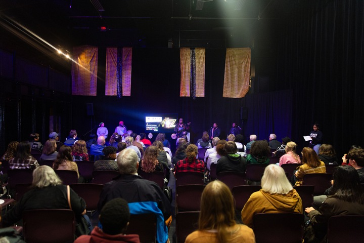 a seated crowd watches a panel of speakers with The Wiz logo on the screen.