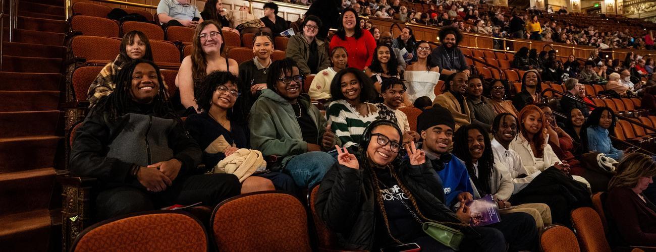 A group of high school students smile at the camera while sitting in their seats at the Benedum Center.