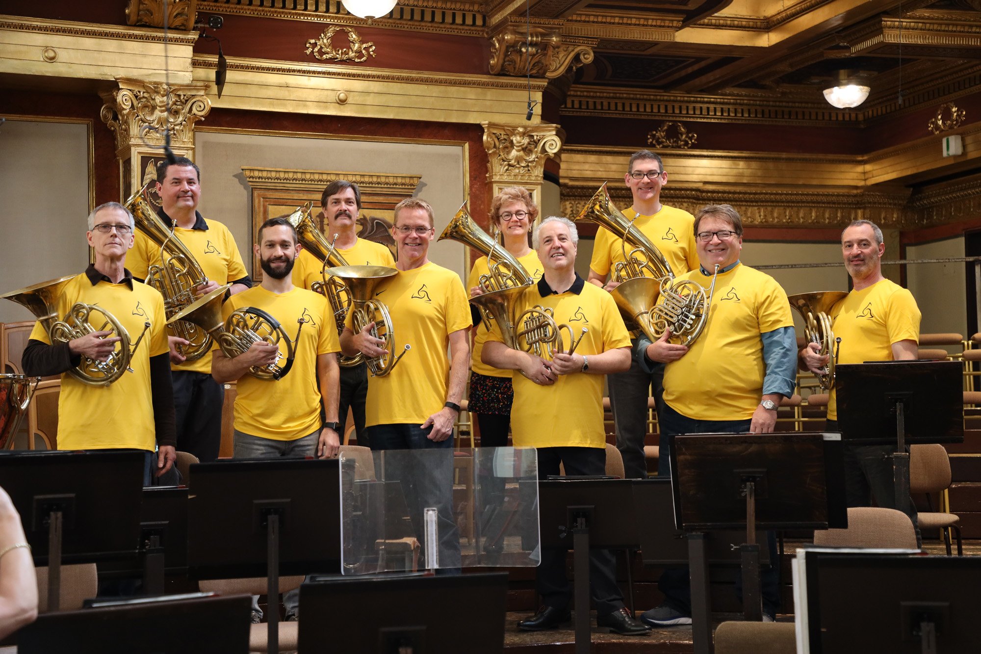 Members of the PSO and Manfred Honeck standing together wearing matching yellow shirts