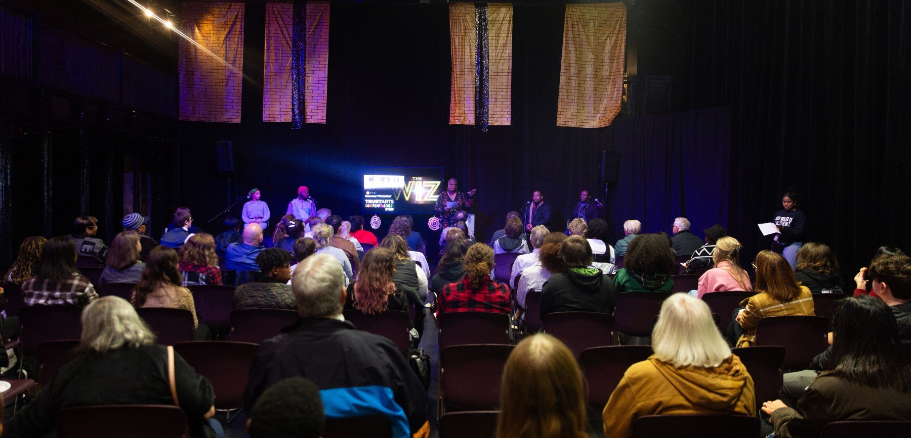 a group of people sit in chairs listening to a presentation given by a woman