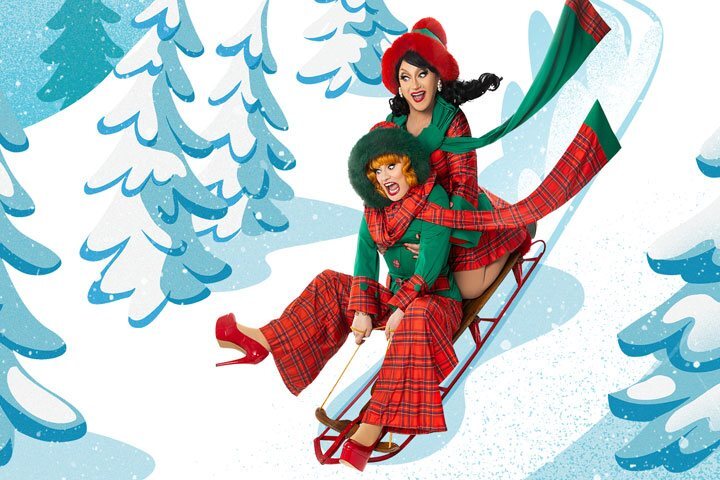 Two drag queens - one red headed and one brunette - are photoshopped onto sled. Behind them is an illustrated blue and white slope with snow-covered trees.