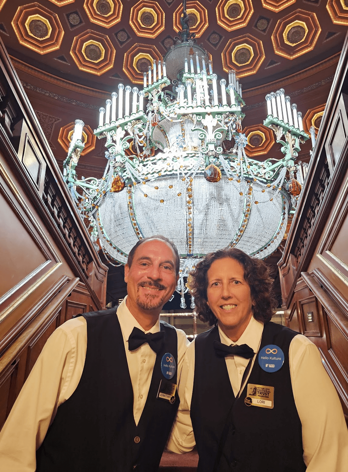 two volunteers pose beneath the crystal chandelier