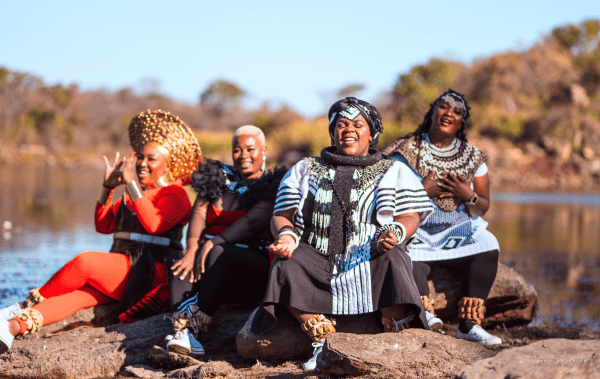 a group of black women sitting on rocks in a natural setting while singing