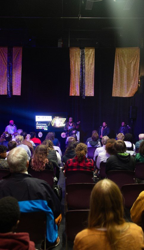 a group of people sit in chairs listening to a presentation given by a woman