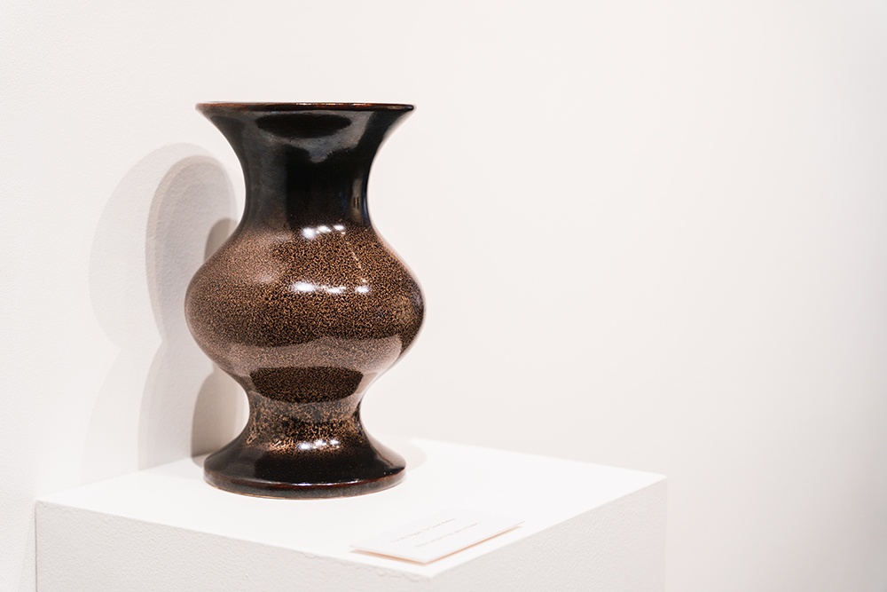 a brown ceramic vase sits on a white plinth