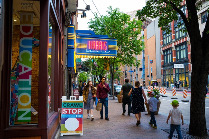 People walking dow the street in front of the Harris Theater marquee and Trust Arts Education Center.