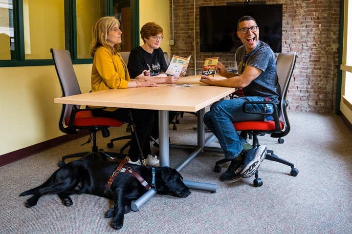 Three people sit at a conference room in an office building, looking over maps on the table.