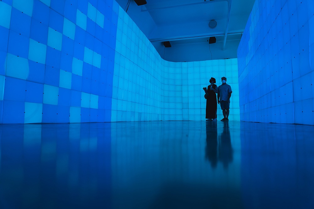 two people stand in a chamber surrounded on all sides by walls of blue light up blocks