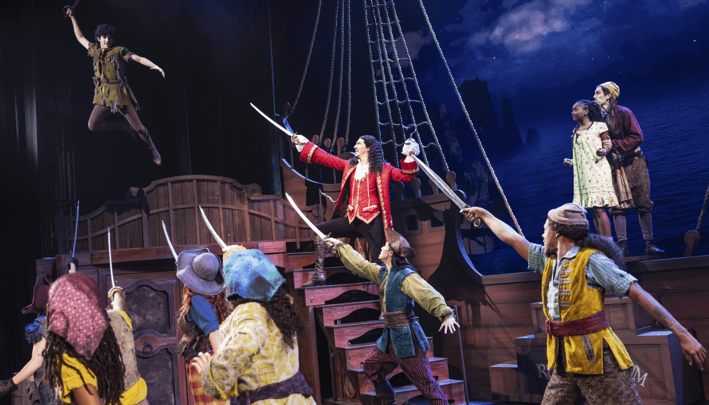 A group of pirates hold up their swords as Peter Pan floats above them.