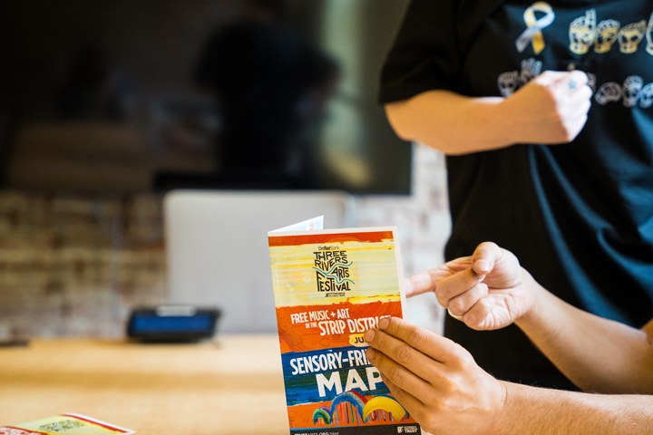  Jonathan points to place in inside the map with Karoline with the background. The map has the Three Rivers Arts Festival logo and the title Sensory Friendly map