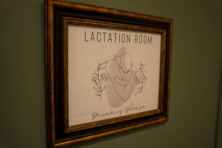 A close up of a print on a green wall. The print says Lactation Room, Privacy Please with a line drawing of person holding a baby.
