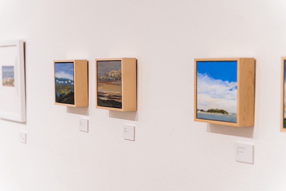 a closeup of three small square landscape paintings hung on a white wall