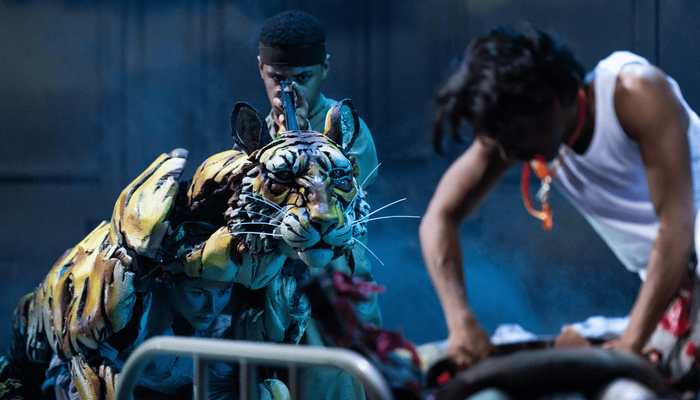 An actor holds up an intricate tiger puppet with one puppeter controlling the animal from the inside.