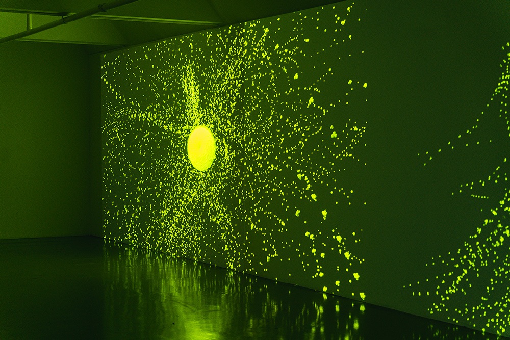 projected green light forms a central circle and splatter pattern on a gallery wall