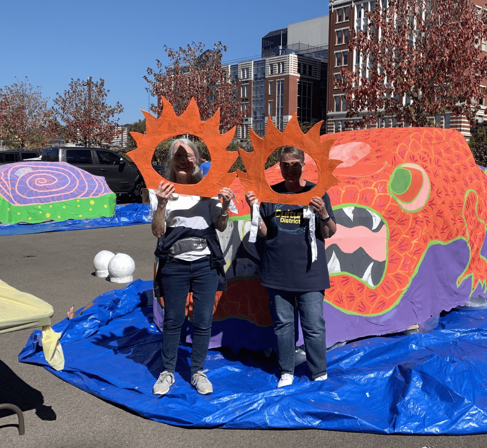 two volunteers decorate a car with orange paper suns for First Night Pittsburgh