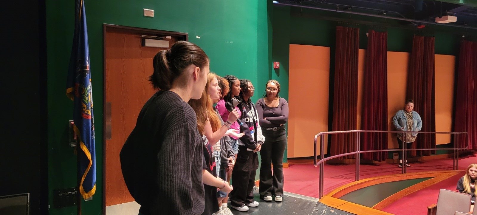 students are lined up in front of the room while one speaks into the microphone