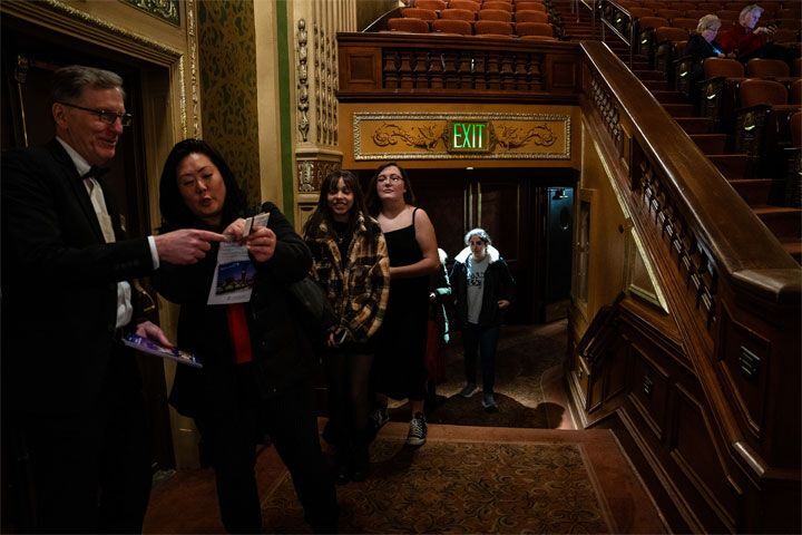 A woman in the Benedum Center auditorium holds up her tickets while an usher points in the direction of their seats.
