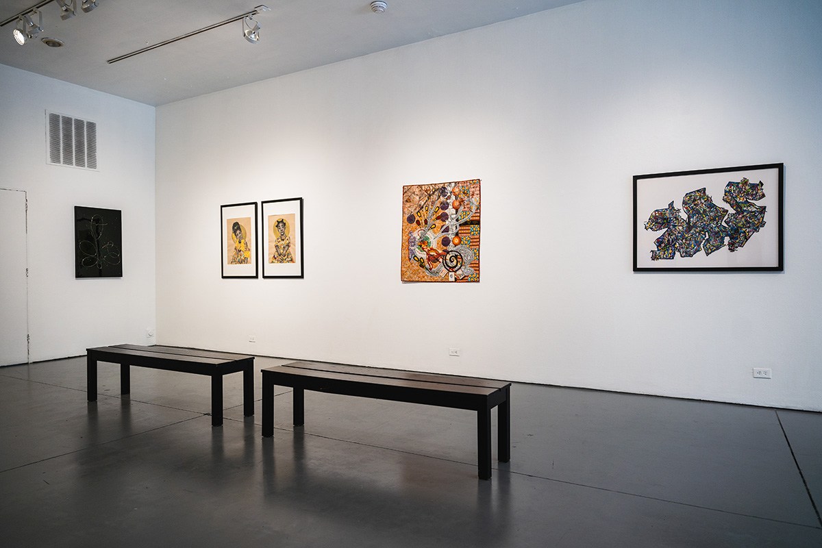 five works hang on a white gallery wall. two black benches sit in the middle of the room.