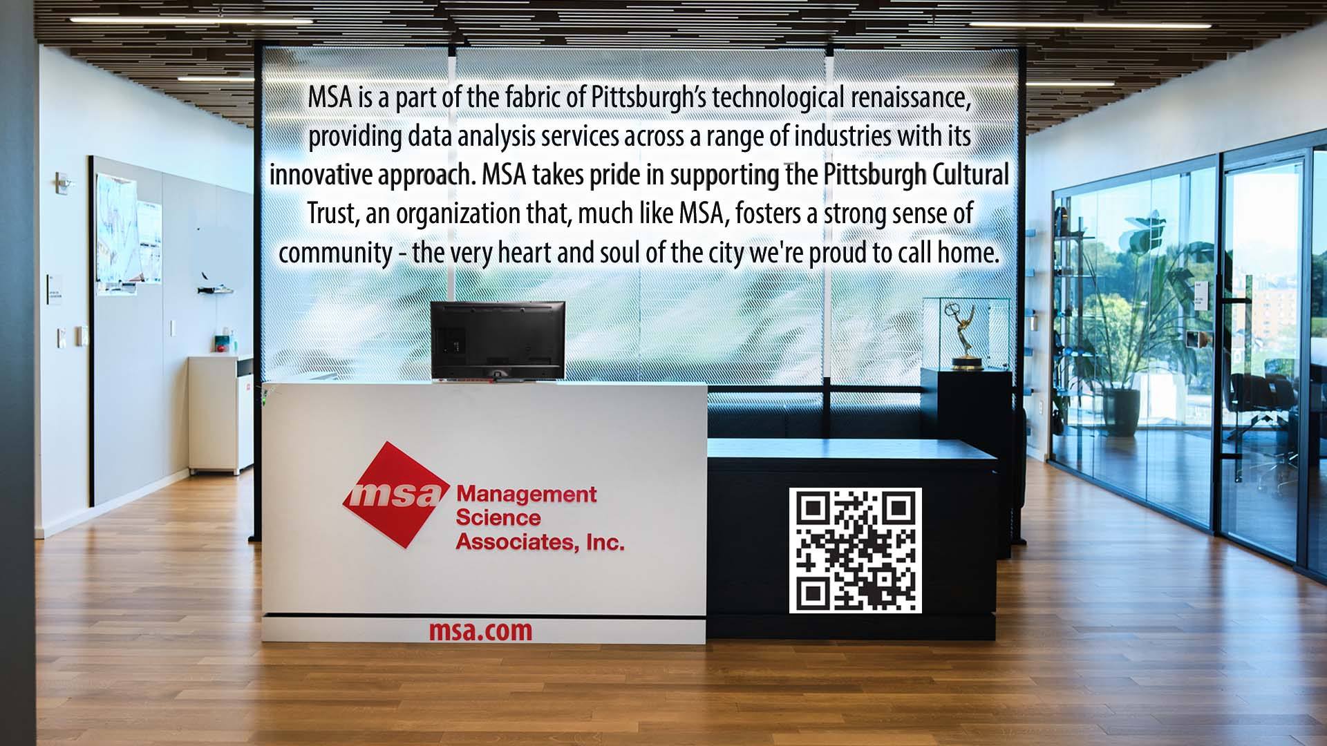 A modern office lobby with a white reception desk featuring the MSA logo, a QR code, and the company’s website. A large window overlooks trees, and a message about MSA’s community involvement is displayed above the desk.