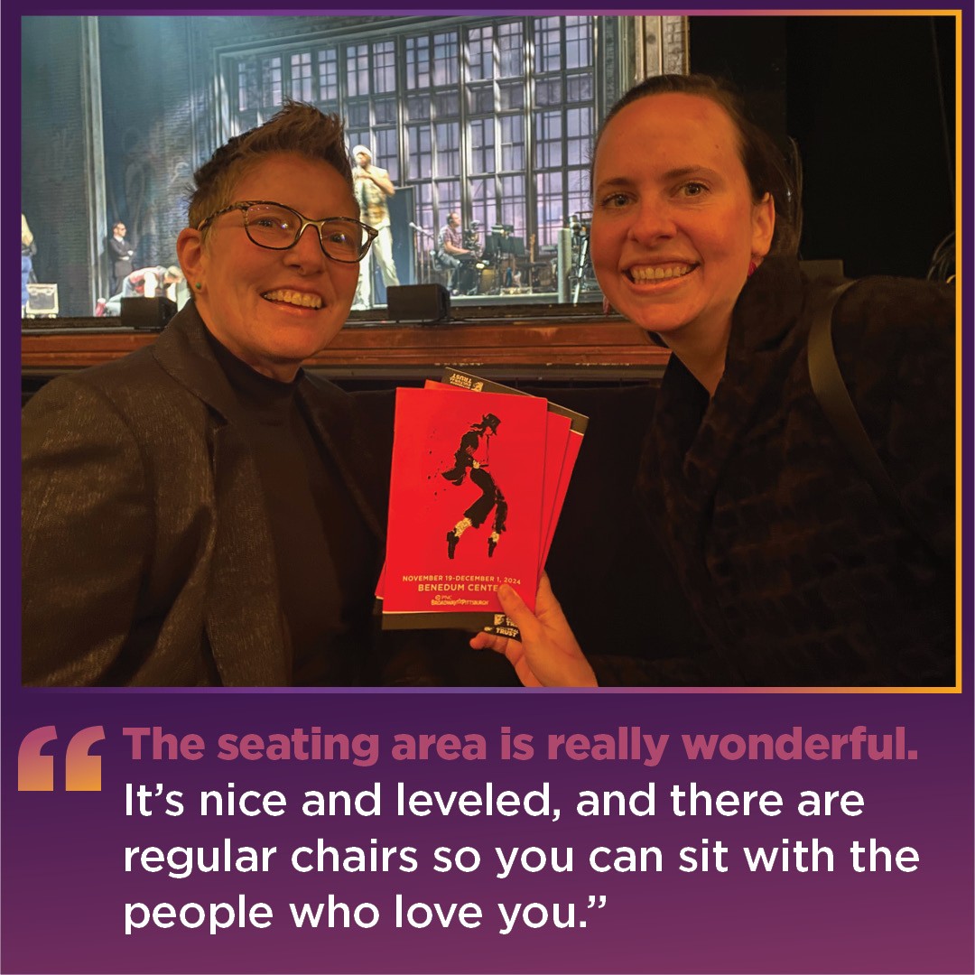 two women, Tess and Allison, hold up their red MJ the Musical programs books. behind them, you can se the stage with the MJ set.