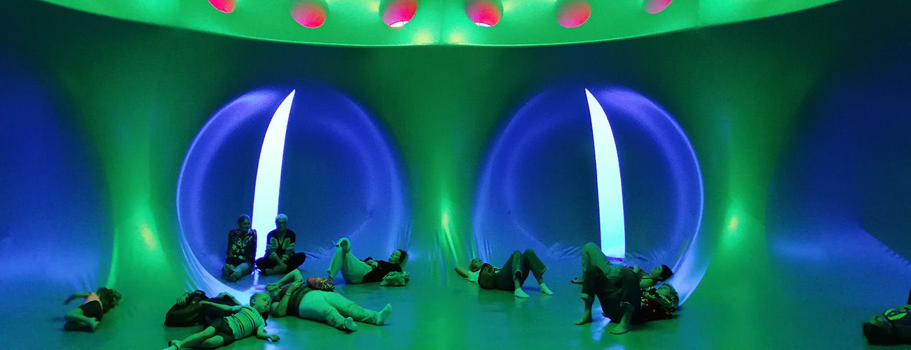 the interior of a large, green inflatable space. a group of people and children all lay on their backs looking up.