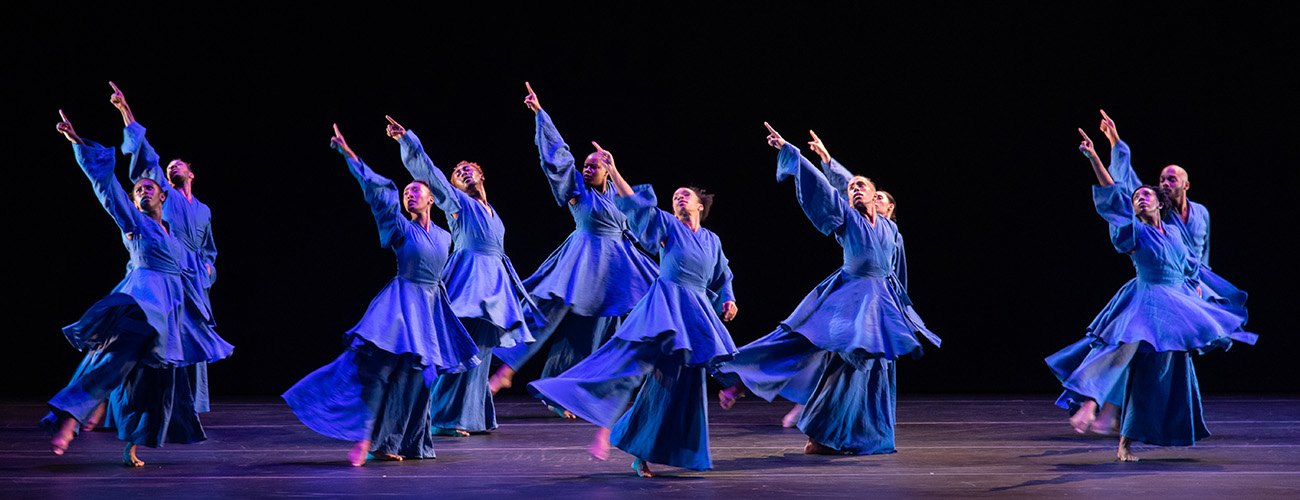 a group of dancers in blue gowns all move together on stage