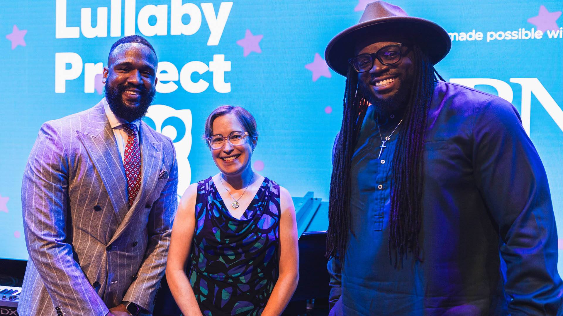 Three people in dress clothes standing in front of a screen smiling at the camera.