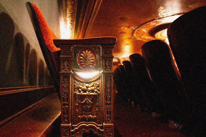 A close up of the side of a Benedum Center seat. The wooden side panel on the side of the seat is ornately carved and a light glows from the middle.