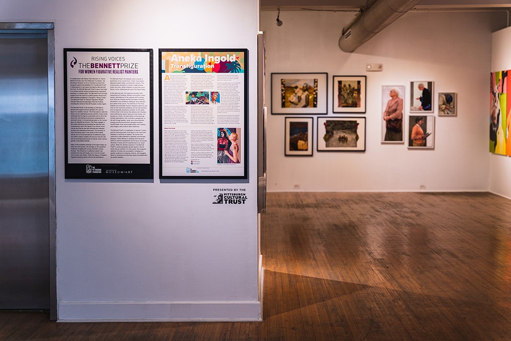 a gallery statement on a white wall in a large gallery space. paintings hang on walls in the distance.