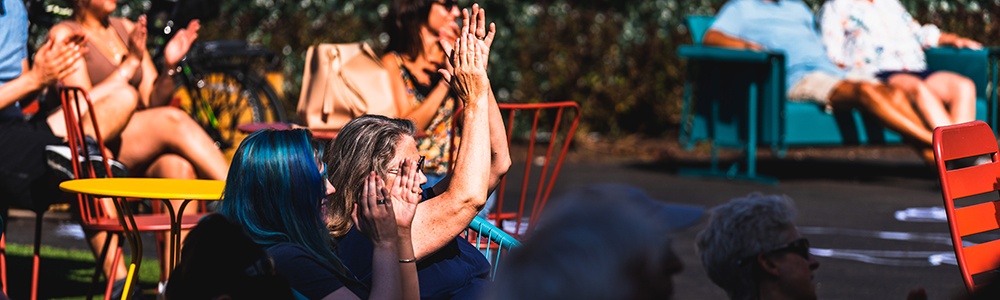 two audience members at a backyard performance holding up their hands and clapping