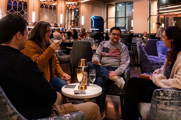 Four people sit around a small, low table in the midst of conversation and a drink in hand.