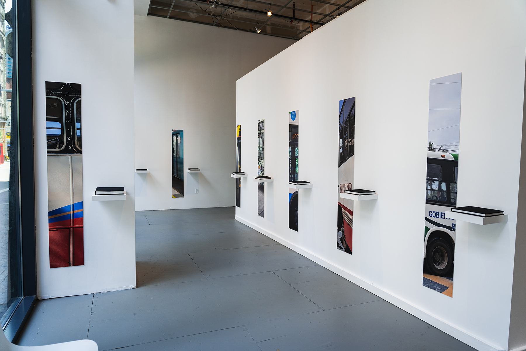a gallery wall with tall, slim slivers of photographs hung next to small ledges. on each ledge is a black book.