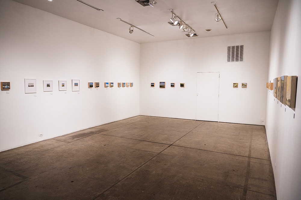 a small gallery space with a single row of small paintings hung around three walls