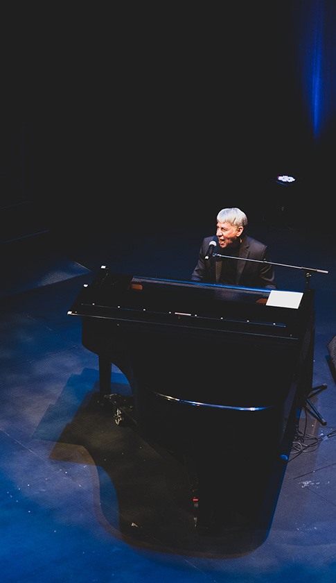 a performer sits at a grand piano and sings into a microphone