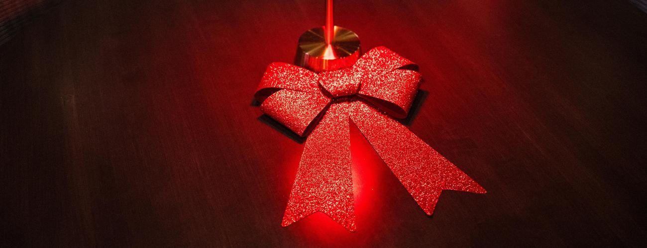  A red sparkling bow rests on a wood table.