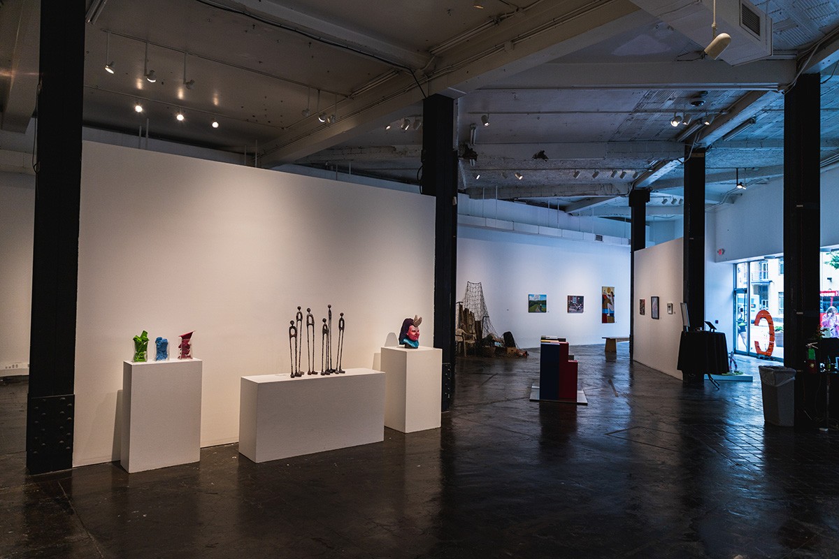 a large industrial gallery space filled with artwork hanging on the walls, sitting on the floor, and perched on pedestals.
