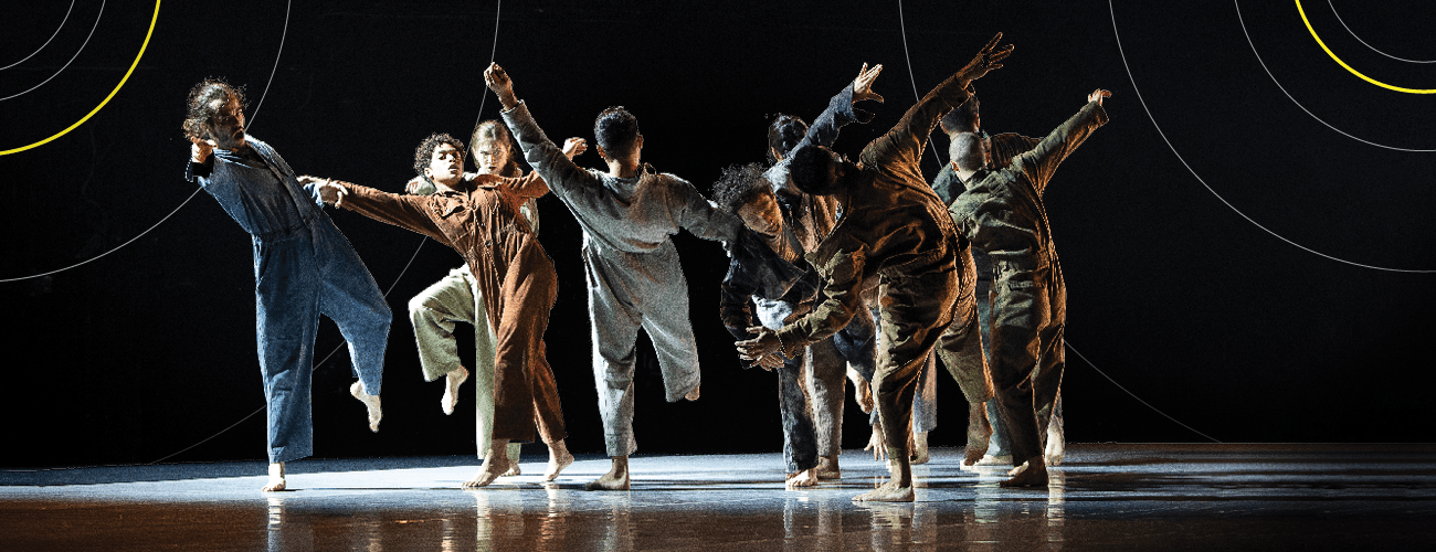 a group of dancers in earth tone jumpsuits all strike a pose with their arms in the air