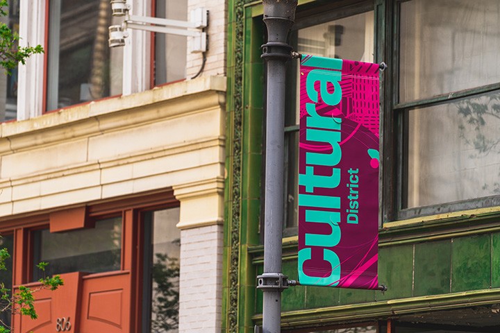 a pink and blue banner that says 'cultural district' hangs from a light pole in front of a building with a green façade
