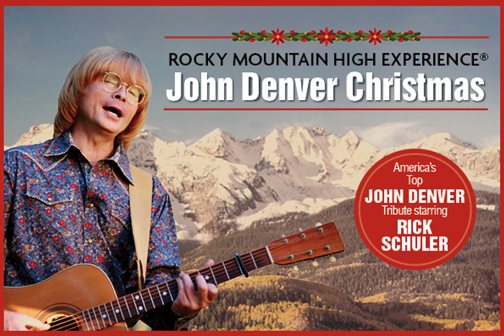 In front of a mountain range, a man in glasses closes his eyes while playing guitar.