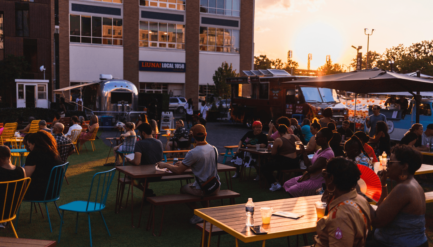 People sit oustide in colorful chairs and around tables as the sun sets.