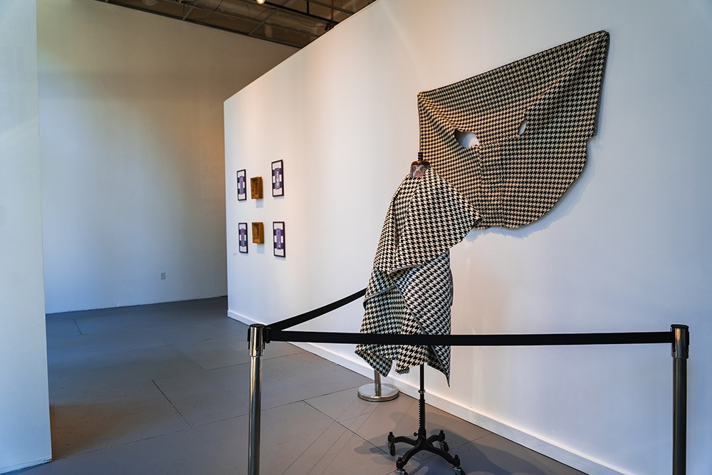 a dress and shawl hang on a mannequin. five paintings hang on a wall in the background.