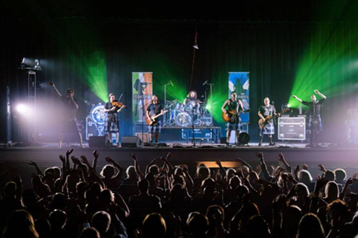 A concert with musicians on stage and green lights with the backs of the audience in the foreground.