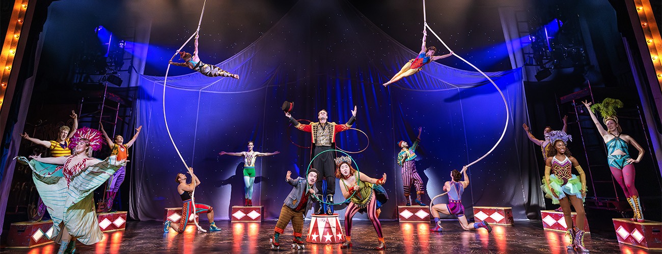 A vibrant circus stage scene with acrobats on ropes, a ringmaster at center, colorful performers in costumes, spotlights, and a starry backdrop, creating a lively and dynamic atmosphere.