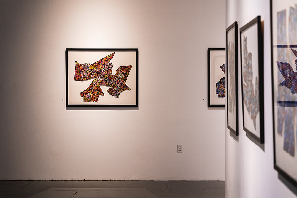 a framed black, orange, and red mixed media piece hangs on a white wall