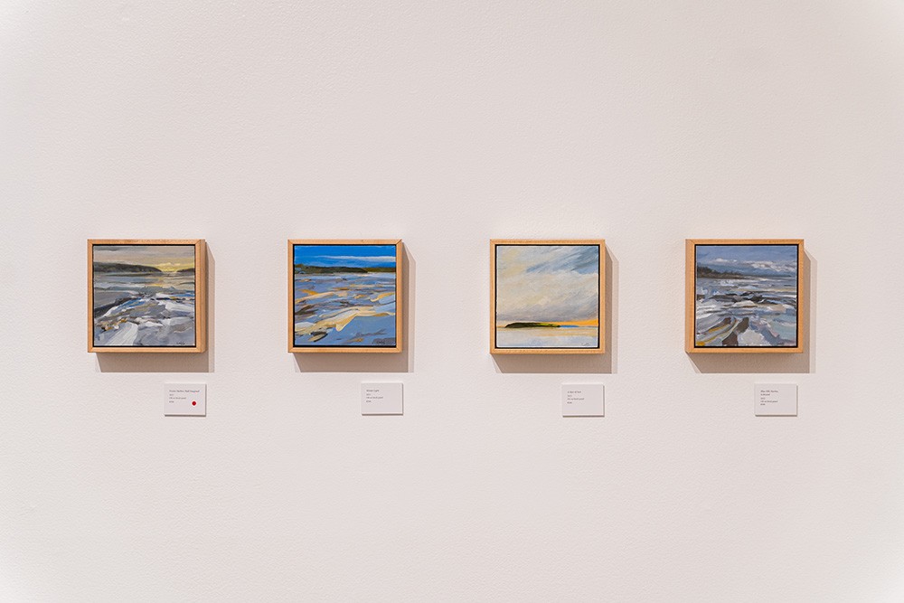 three small square paintings of beach scenes hung in a line on a white wall