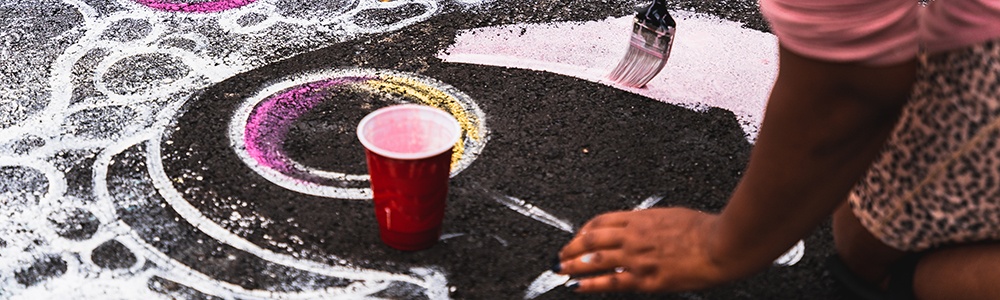 a detail shot of two hands painting pink and white bubbles on black asphalt
