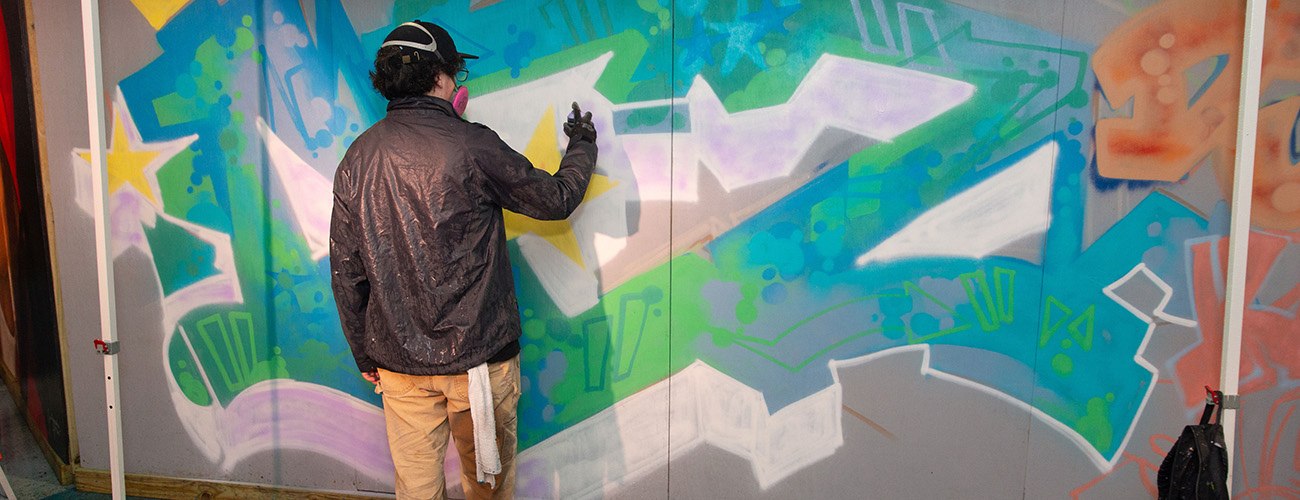 a man in a gray jacket spray painting a colorful graffiti mural