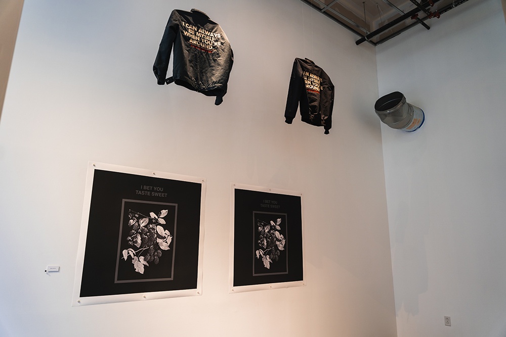 two black and white prints hang on a white wall. two black leather jackets hang from the ceiling above them